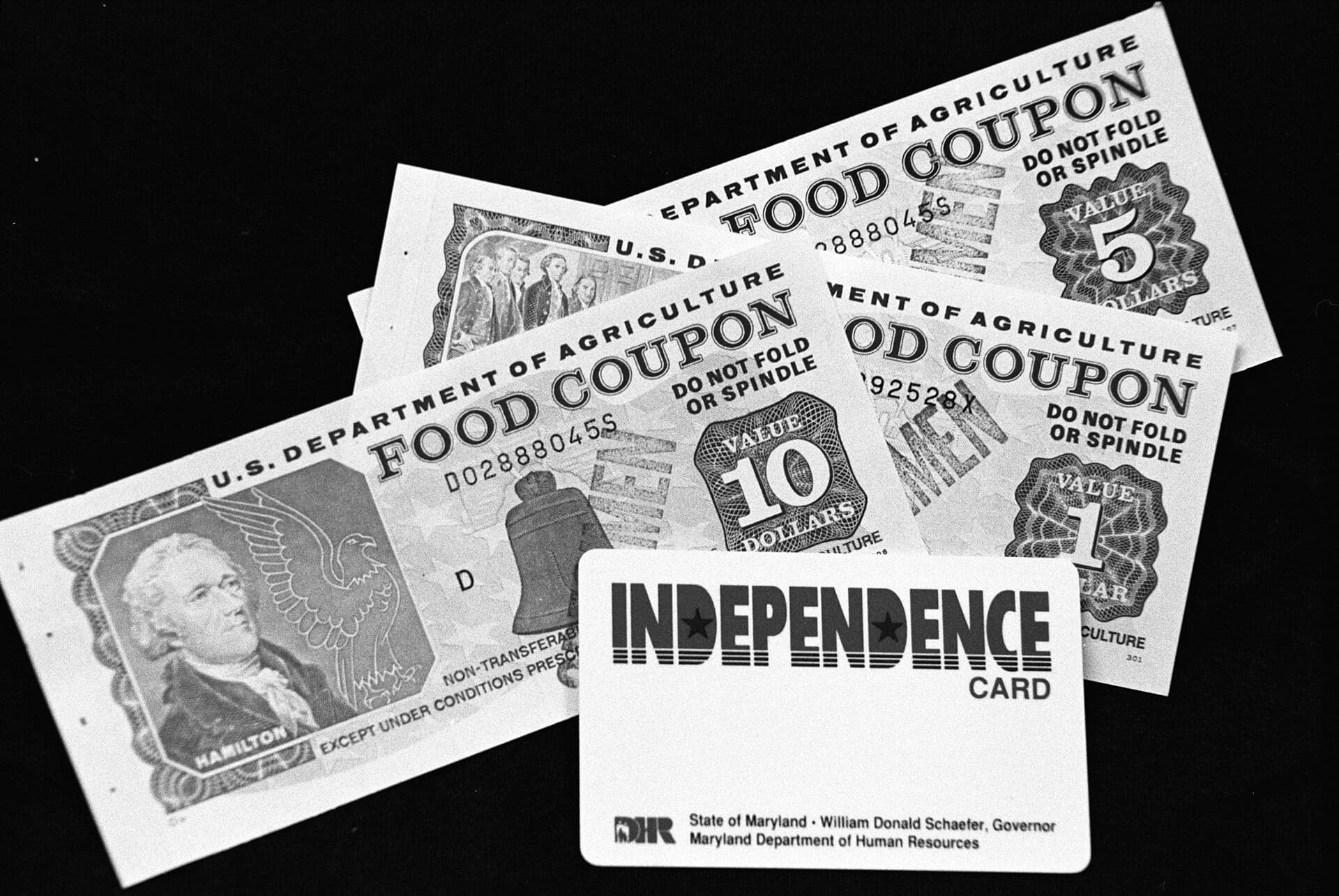 Paper food coupons in 1, 5 and 10 dollar values beside an early EBT card