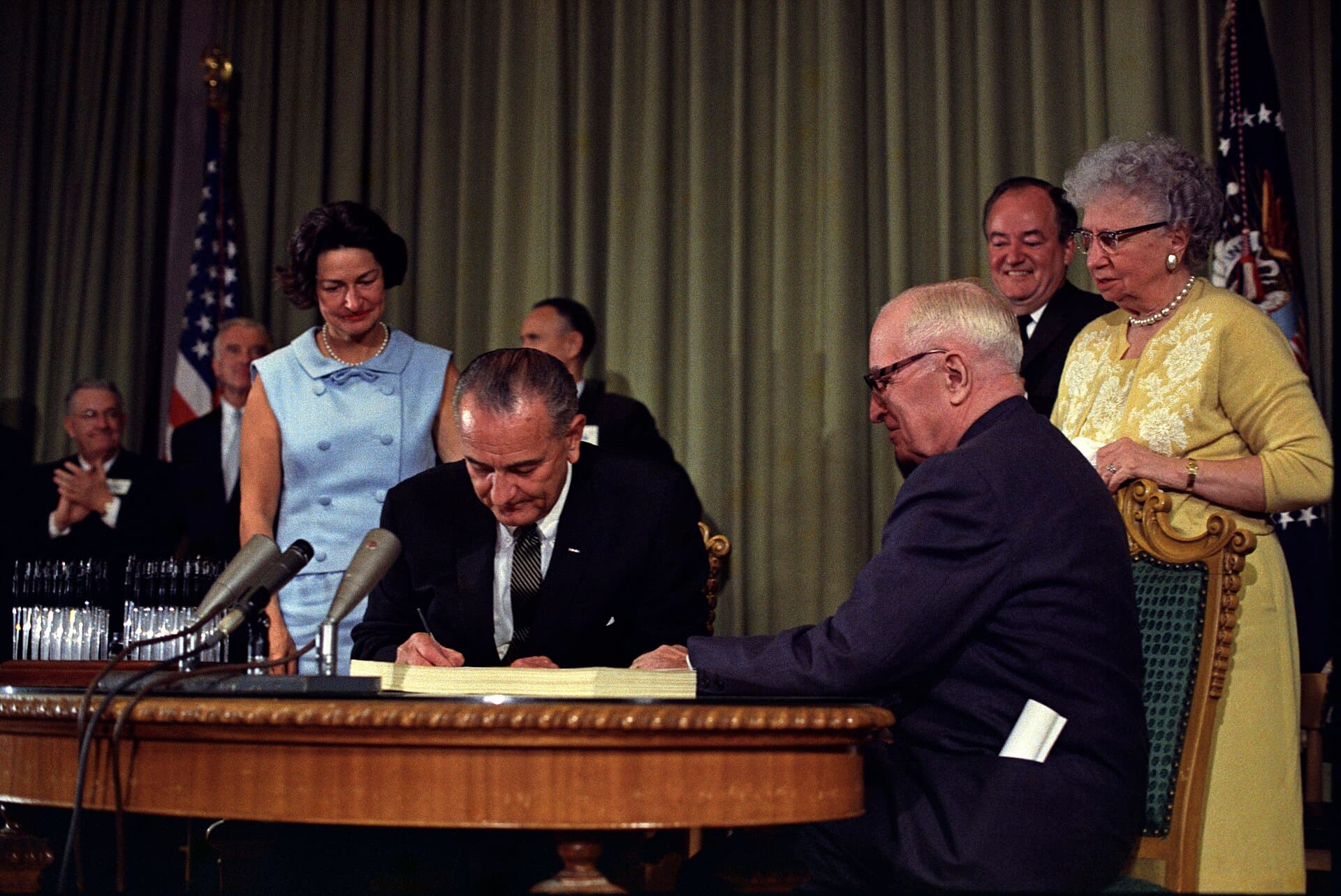 President Lyndon Johnson signs the 1965 Medicare and Medicaid bill beside Harry Truman