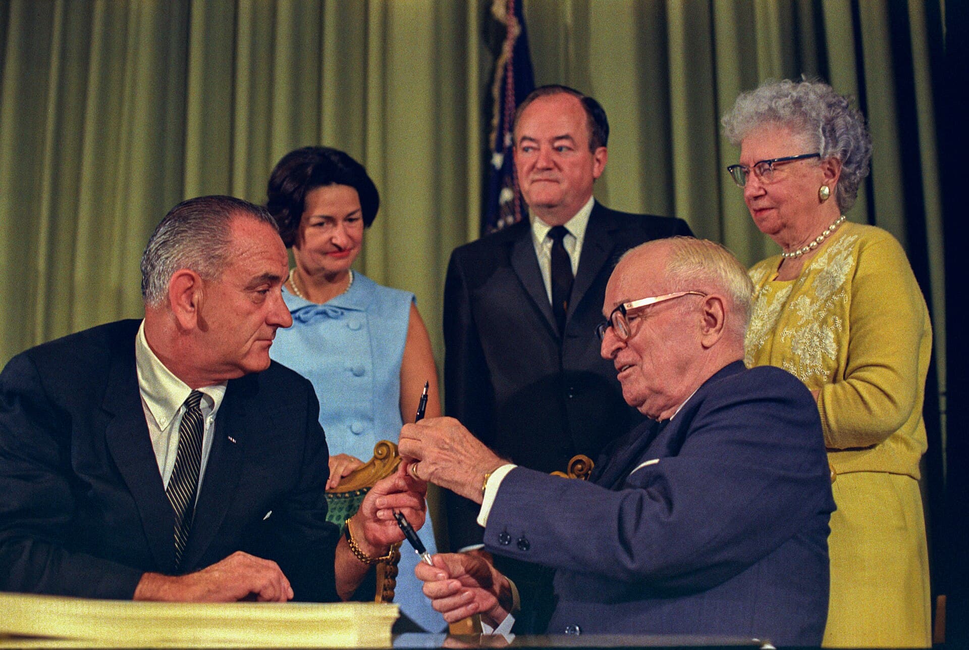 Lyndon Johnson hands Harry Truman a signing pen