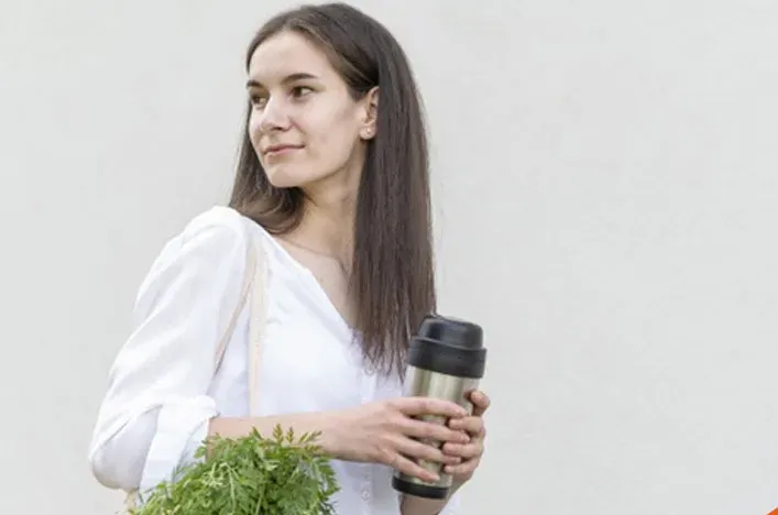 A young woman carrying a bag of fresh vegetables and a drink