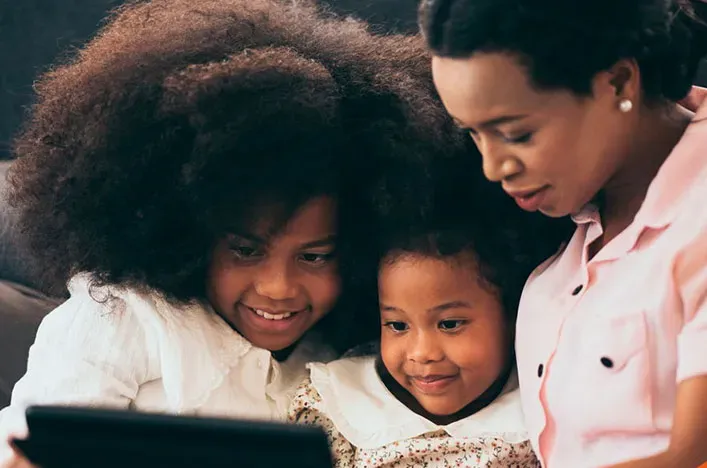 A mother and her two daughters looking at a tablet together
