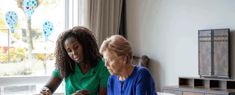 A caregiver doing a puzzle with an older woman at a kitchen table