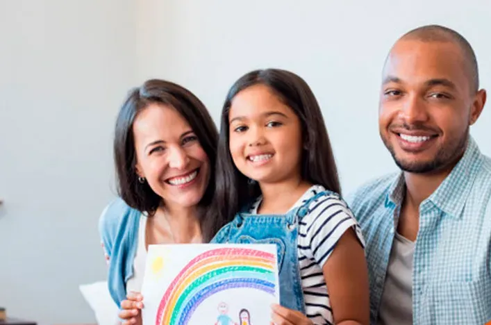 Smiling parents with their daughter holding a drawing of a family