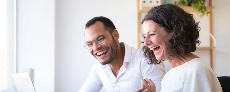 A couple laughing while going over their paperwork at a laptop