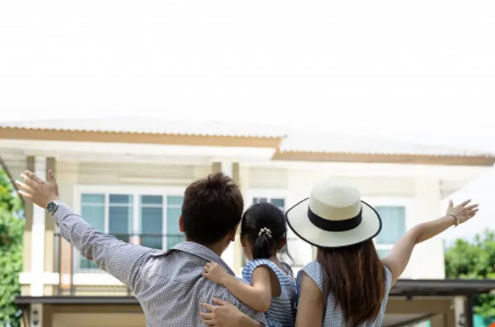 A family with their arms up in front of a new home