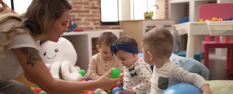 A mother playing with three toddlers on a colorful playroom floor